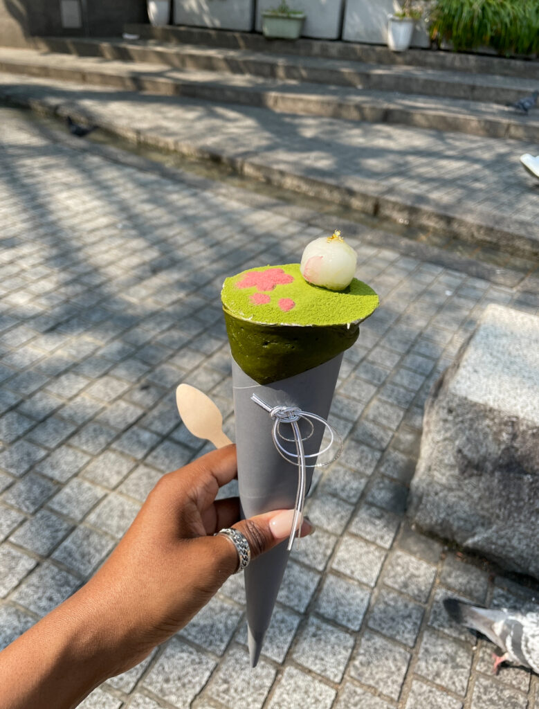 Hand holding a matcha dessert cone with pink flower detail and a white mochi ball on top.