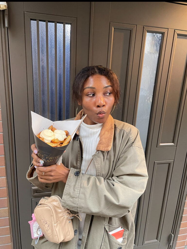 Woman holding a cone of French fries with sauces in front of a Kyoto street door.