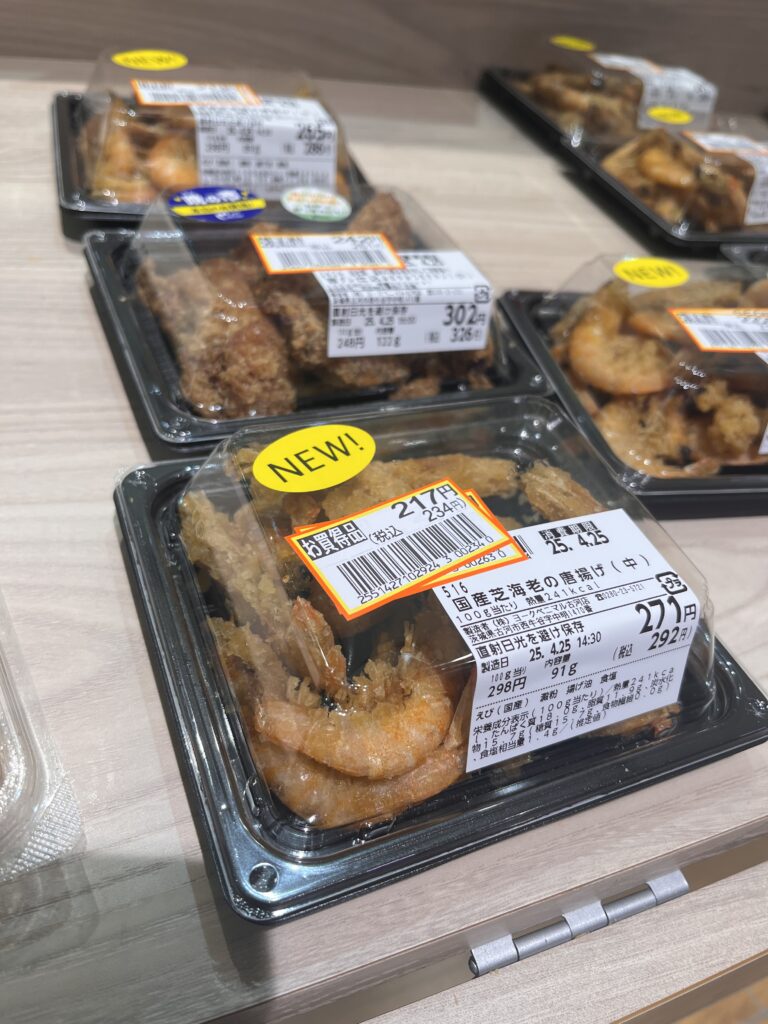 Discounted fried food bento trays in a Japanese grocery store, including deep-fried shrimp and karaage chicken, marked with yellow and orange discount labels.