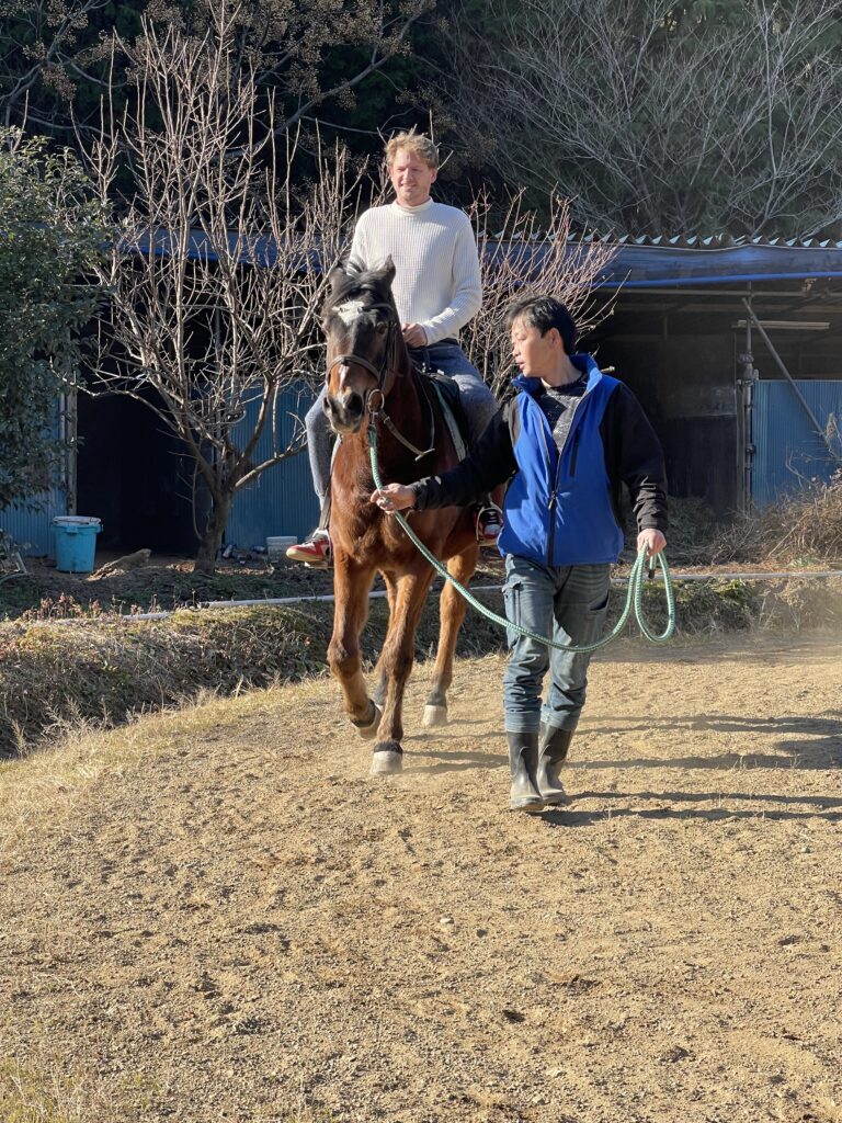 Christopher riding a horse led by a local guide on a dirt path surrounded by trees.
