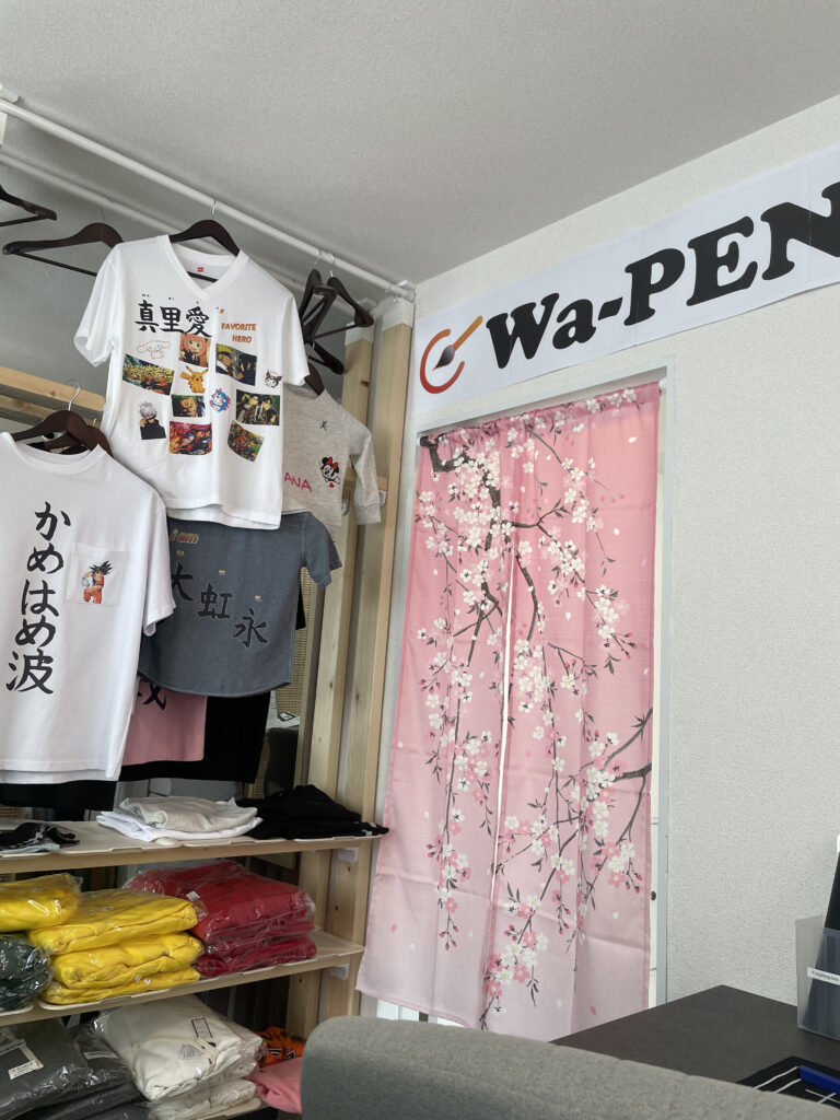 Interior of Wa-Pen Calligraphy shop with custom t-shirts on display and a pink noren curtain with cherry blossoms.