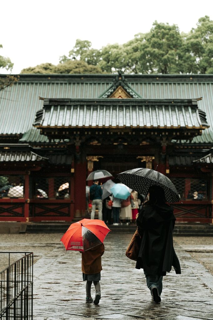 A child and adult holding umbrellas in front of a Japanese temple