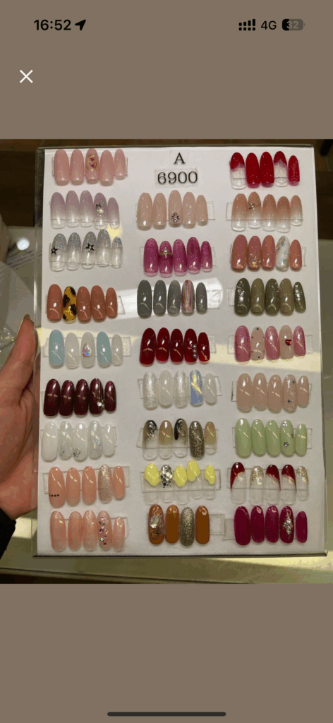 Display board of sample gel nail designs at a Japanese salon, showing various styles and colors with a ¥6,900 price label.
