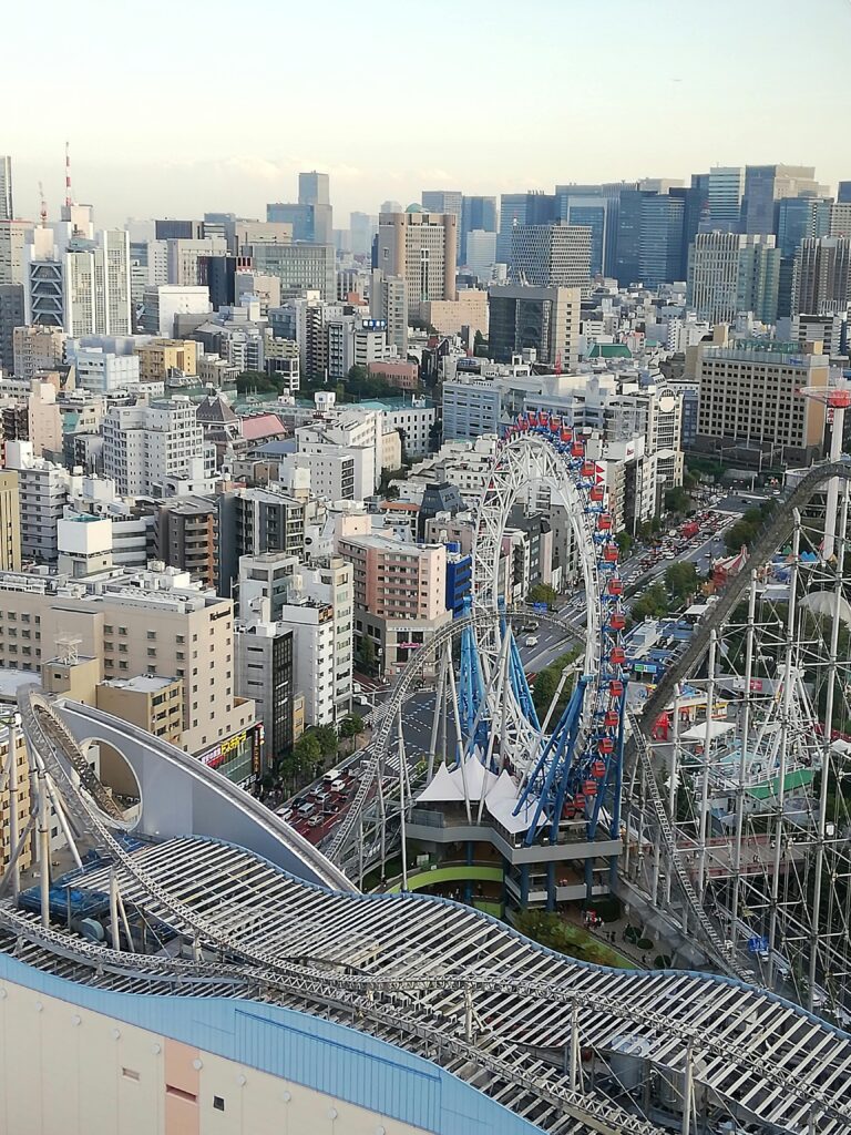Rollercoaster and Ferris wheel surrounded by buildings in the heart of Tokyo Dome City.