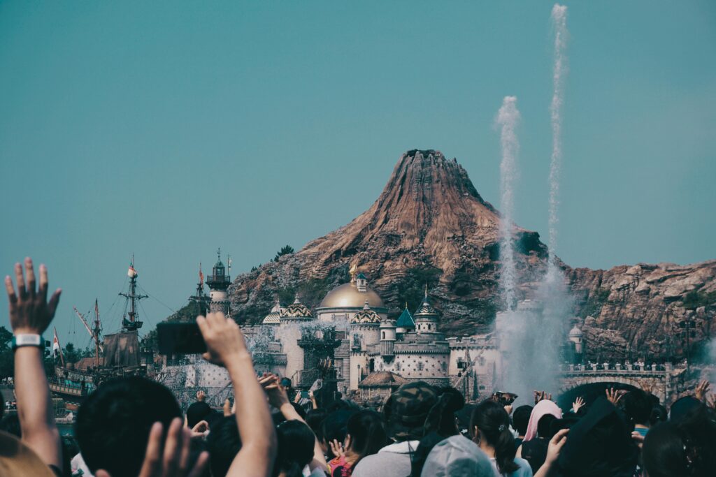 Crowd cheering during a show at Tokyo DisneySea with a volcanic mountain and castle-like buildings in the background.