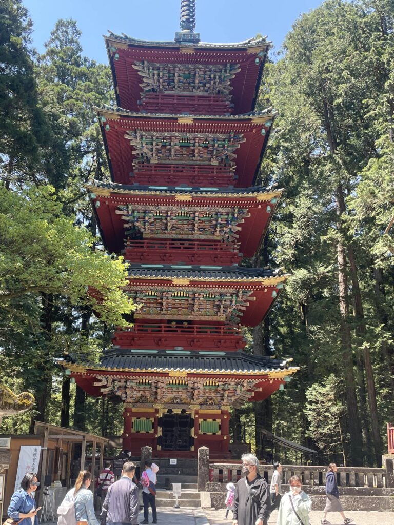 A tall, vibrant red five-story pagoda surrounded by tall cedar trees in Nikko.
