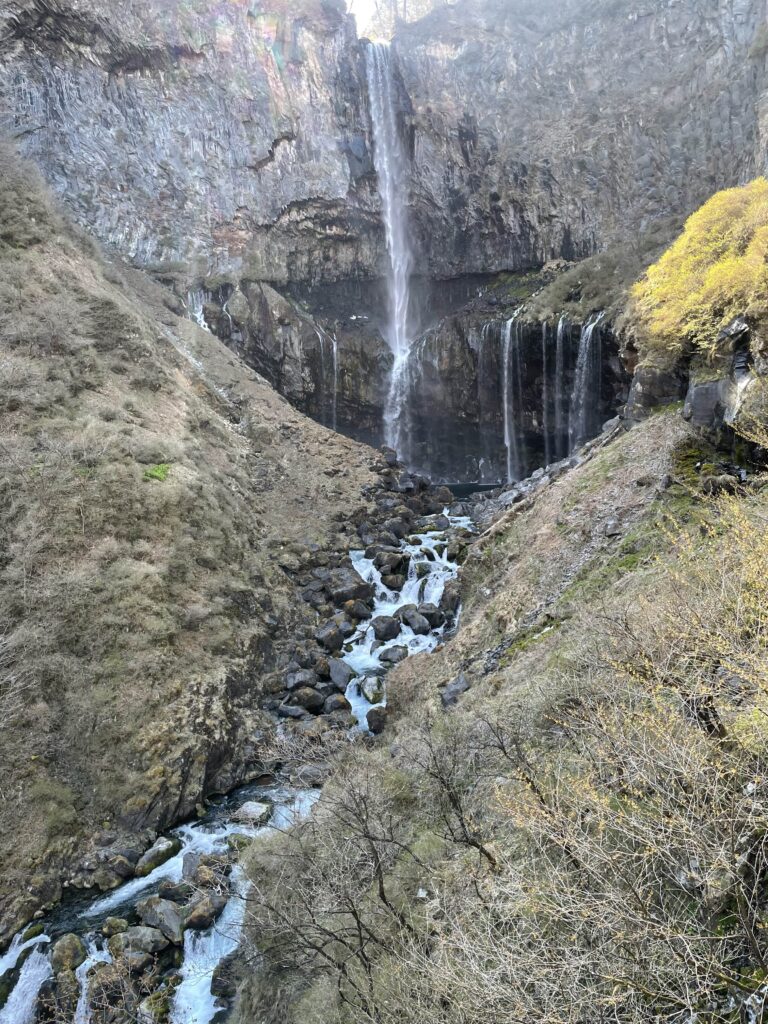 A wide view of Kegon Falls with water streaming down a steep cliff into rocky terrain.