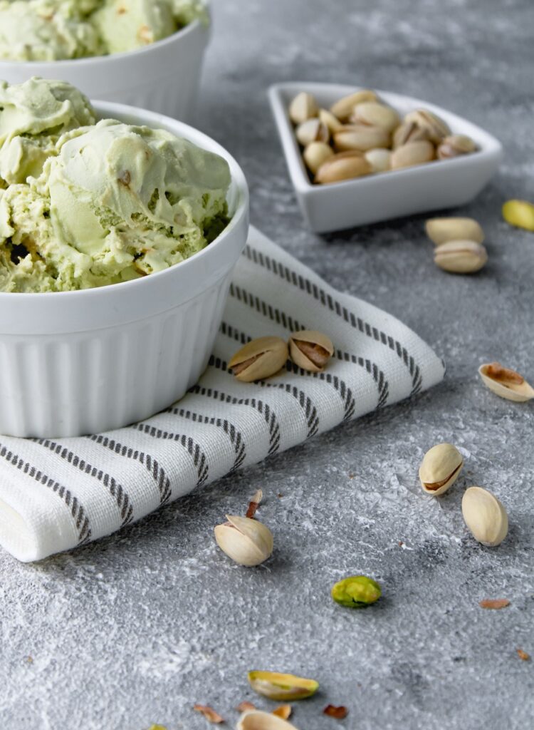 Bowl of pistachio ice cream with scattered pistachios on a striped cloth.