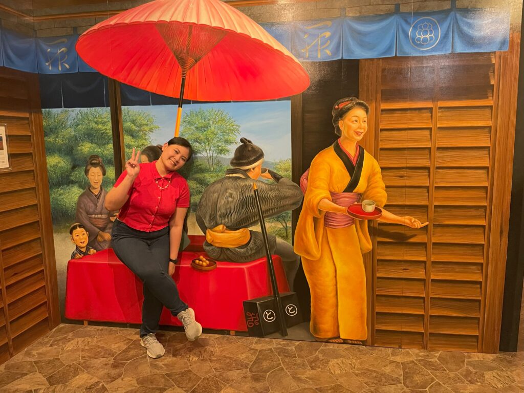 A woman posing under a traditional umbrella among illusionary tea house figures.