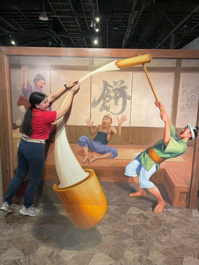  A woman pulling a giant mochi being pounded by another character in a traditional Japanese setting.