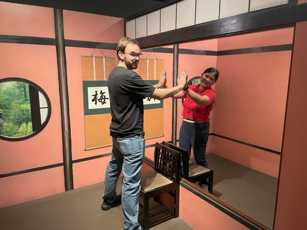A man and woman facing each other as if touching through a mirror illusion in a traditional Japanese room.