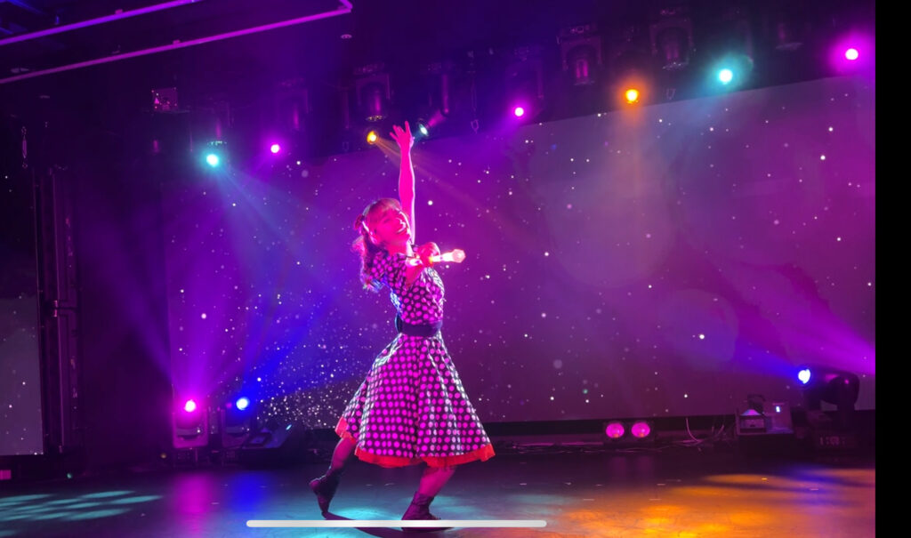 Performer in a polka dot dress dancing on stage with bright lights
