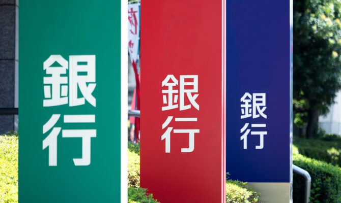 Vertical signs with the kanji for “bank” (銀行) outside different Japanese banks in green, red, and blue.