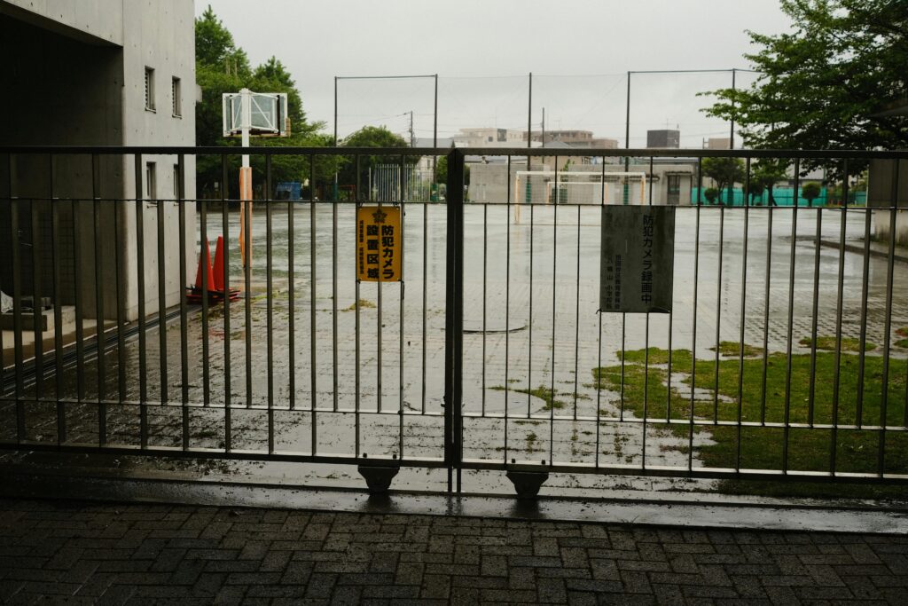 Closed school grounds seen through a gate on a rainy day in Japan.