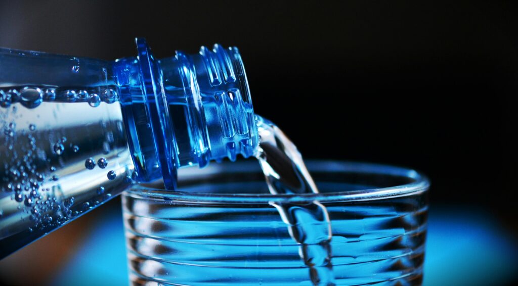 Close-up of a plastic water bottle pouring water into a glass with a dark background.