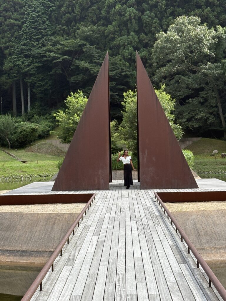 A visitor walking through a tall triangular steel sculpture at Morou Art Forest in Nara.