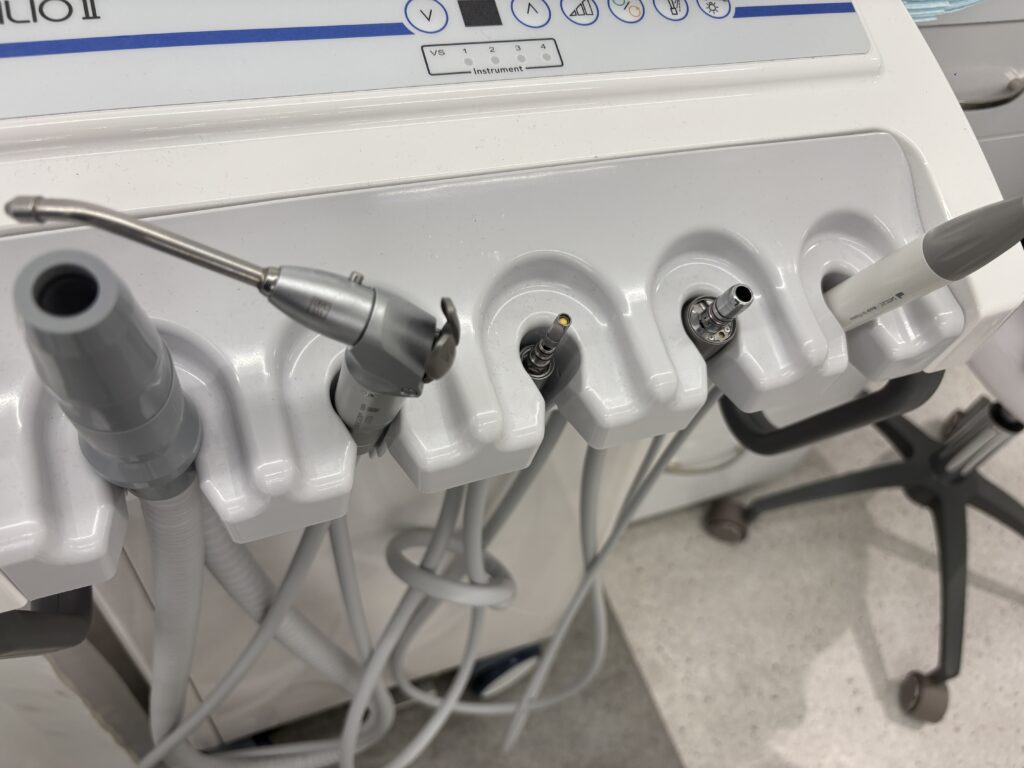 A white dental unit with multiple dental tools including air and water nozzles and a high-speed handpiece, neatly organized in a clinical setting.