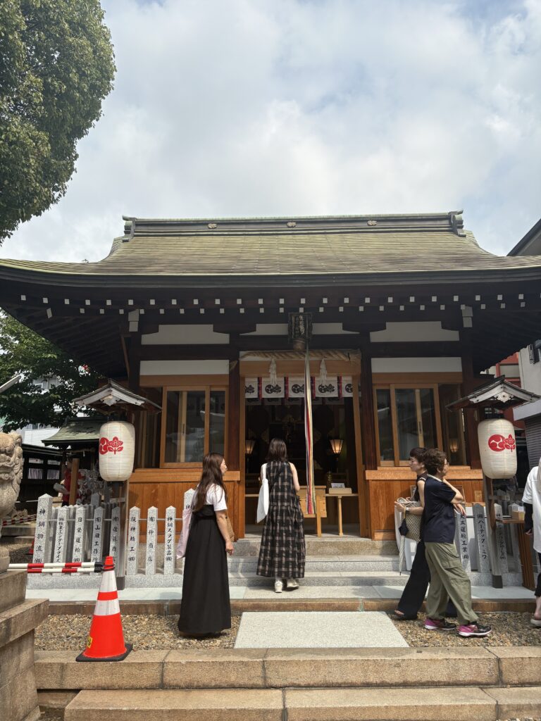 People waiting under umbrellas in a long, organized line marked with red cones outside Wakinohama Shrine.