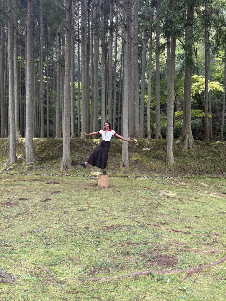 A visitor playfully posing among tall cedar trees at Morou Art Forest.