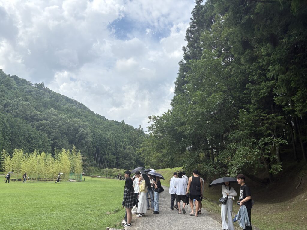 Group of visitors walking with umbrellas along a forest path at Morou Art Forest.