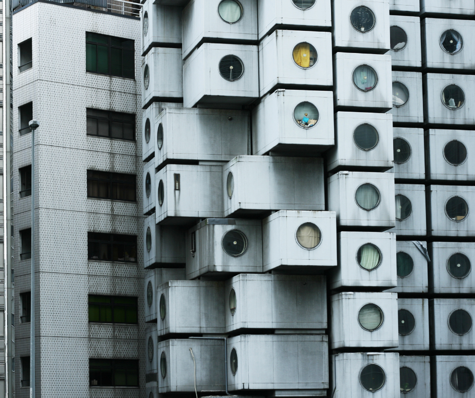 Exterior view of the Nakagin Capsule Tower in Tokyo, showing stacked concrete pods with round windows.