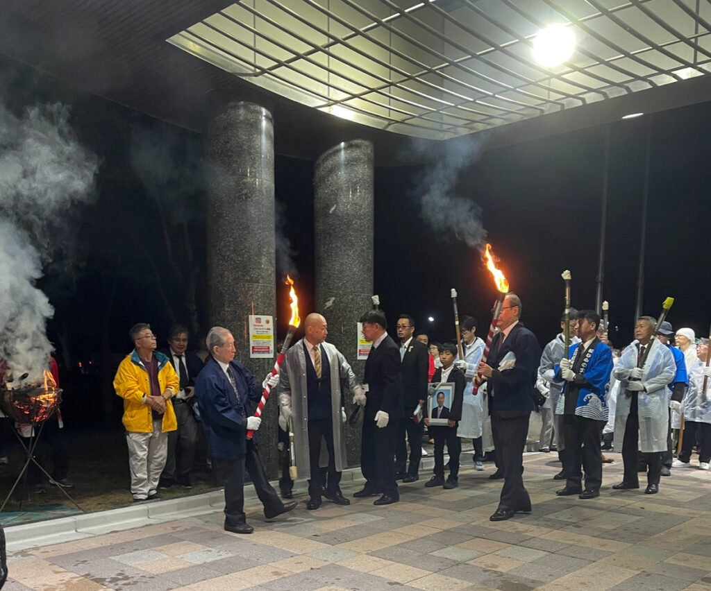 Torchbearers lining up with fire torches outside a hall.