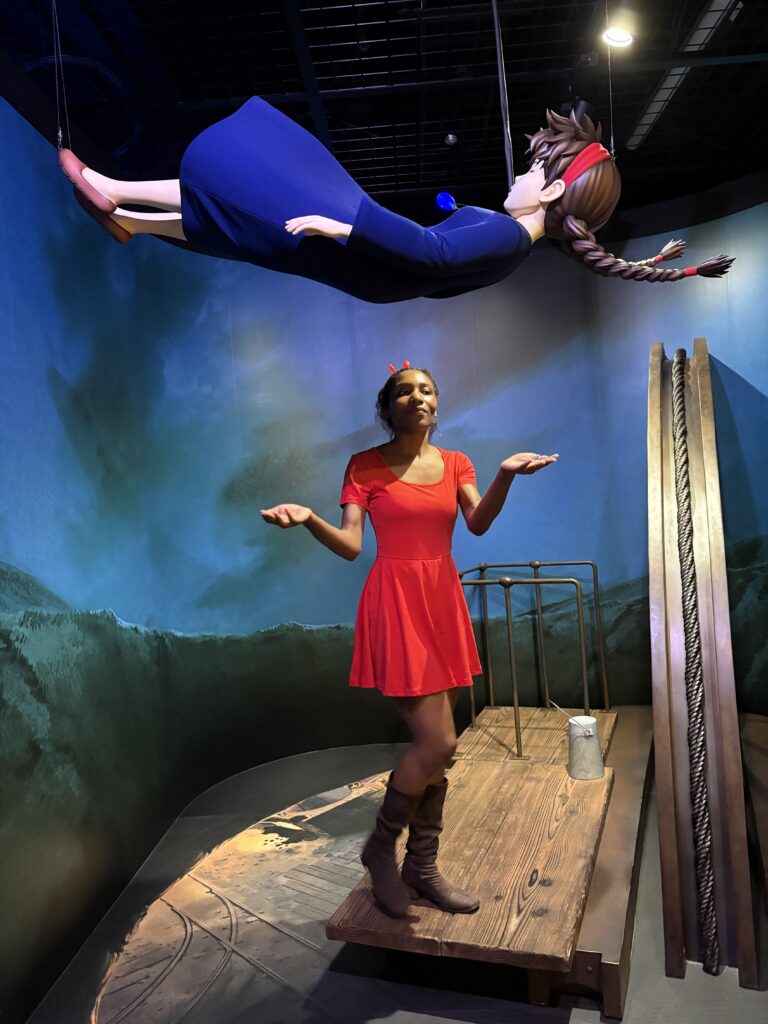 Visitor standing under a suspended figure from Nausicaä of the Valley of the Wind, striking a playful pose.
