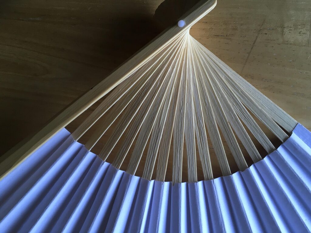A close view of a traditional paper fan with bamboo spokes spread open.
