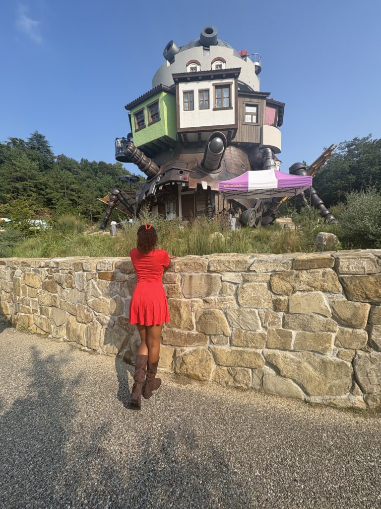 Visitor in a red dress looking up at the life-sized Howl’s Moving Castle replica in Valley of Witches.