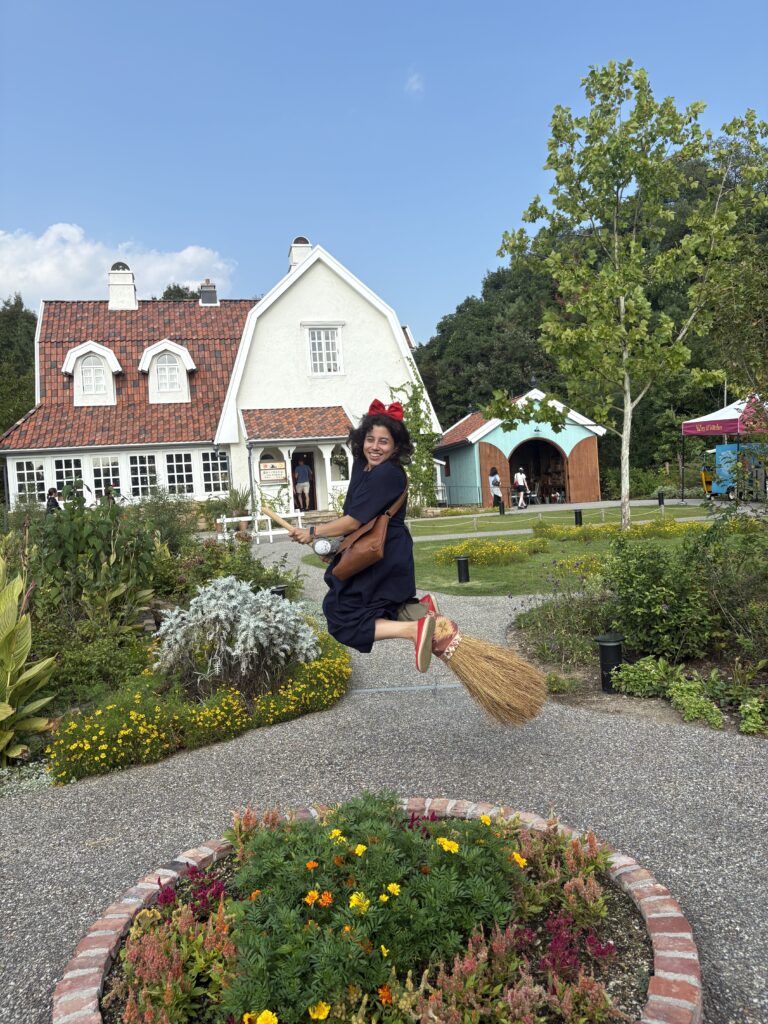 Guest dressed as Kiki from Kiki’s Delivery Service jumping on a broomstick for a playful photo in front of a cottage.