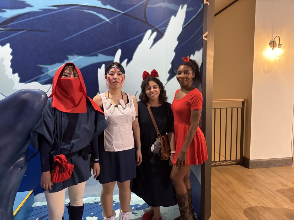 Group of cosplayers posing together at Ghibli Park, including Kiki, San from Princess Mononoke, and other characters.