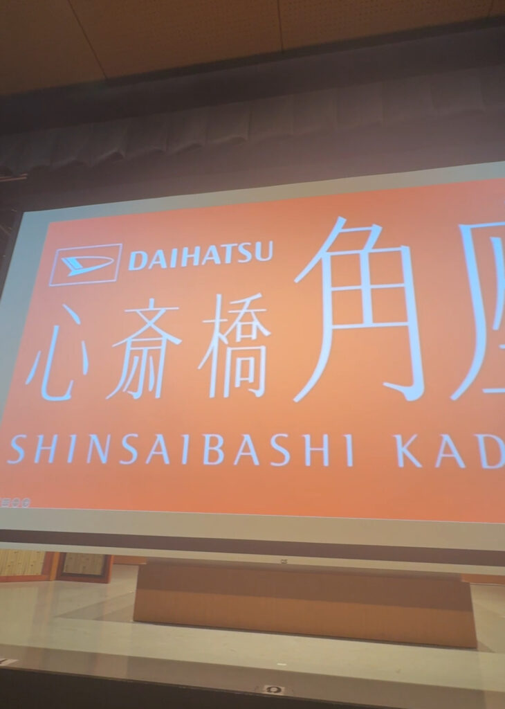 Large orange screen displaying “DAIHATSU Shinsaibashi Kadoza” in Japanese and English inside the theatre.