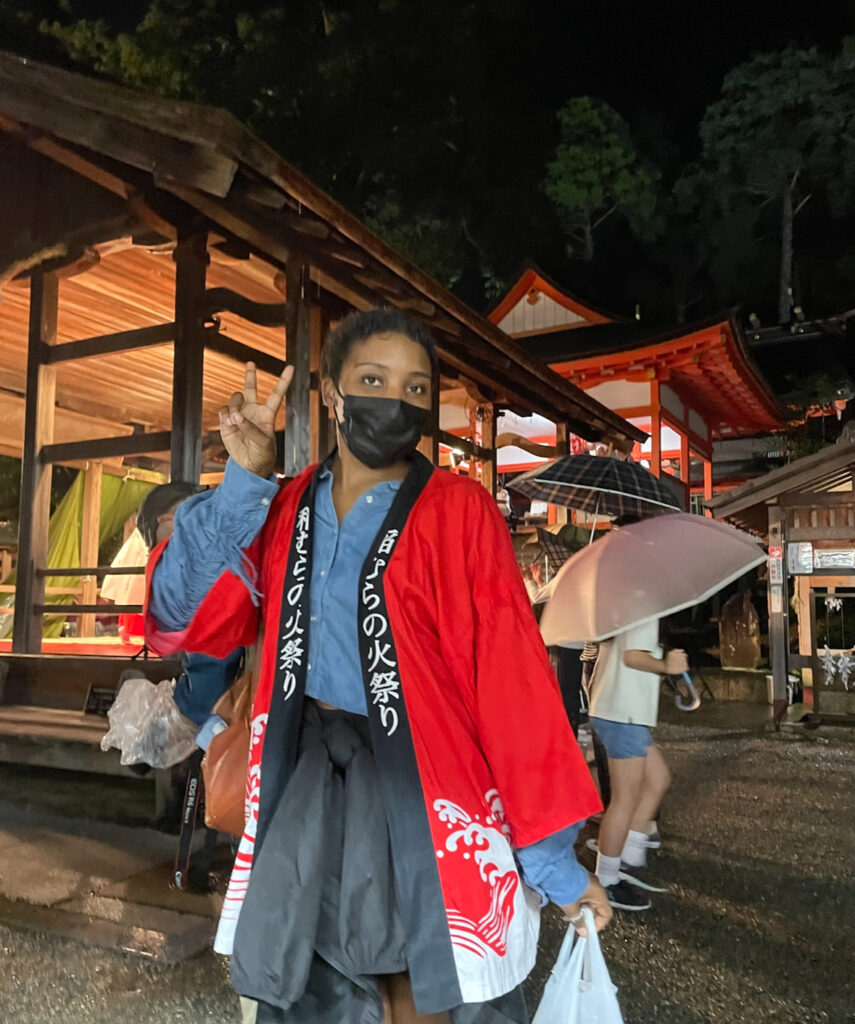 Festival participant in red happi coat posing with a peace sign.
