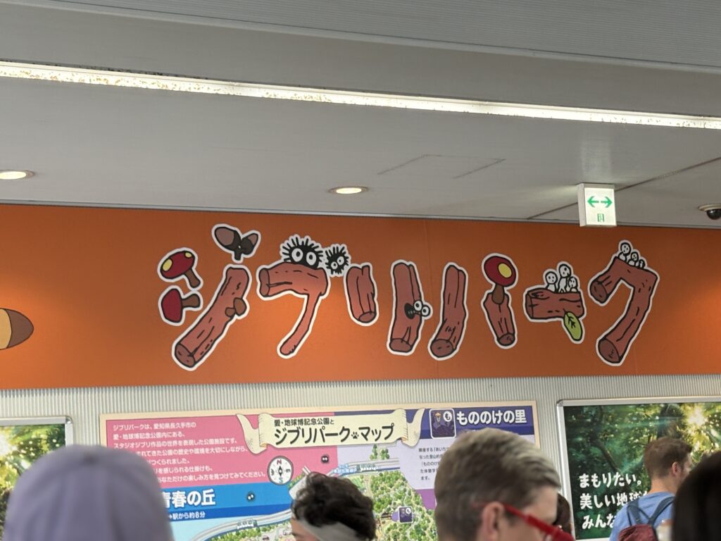 Bright orange “Ghibli Park” sign decorated with soot sprites and Kodama above the info area.