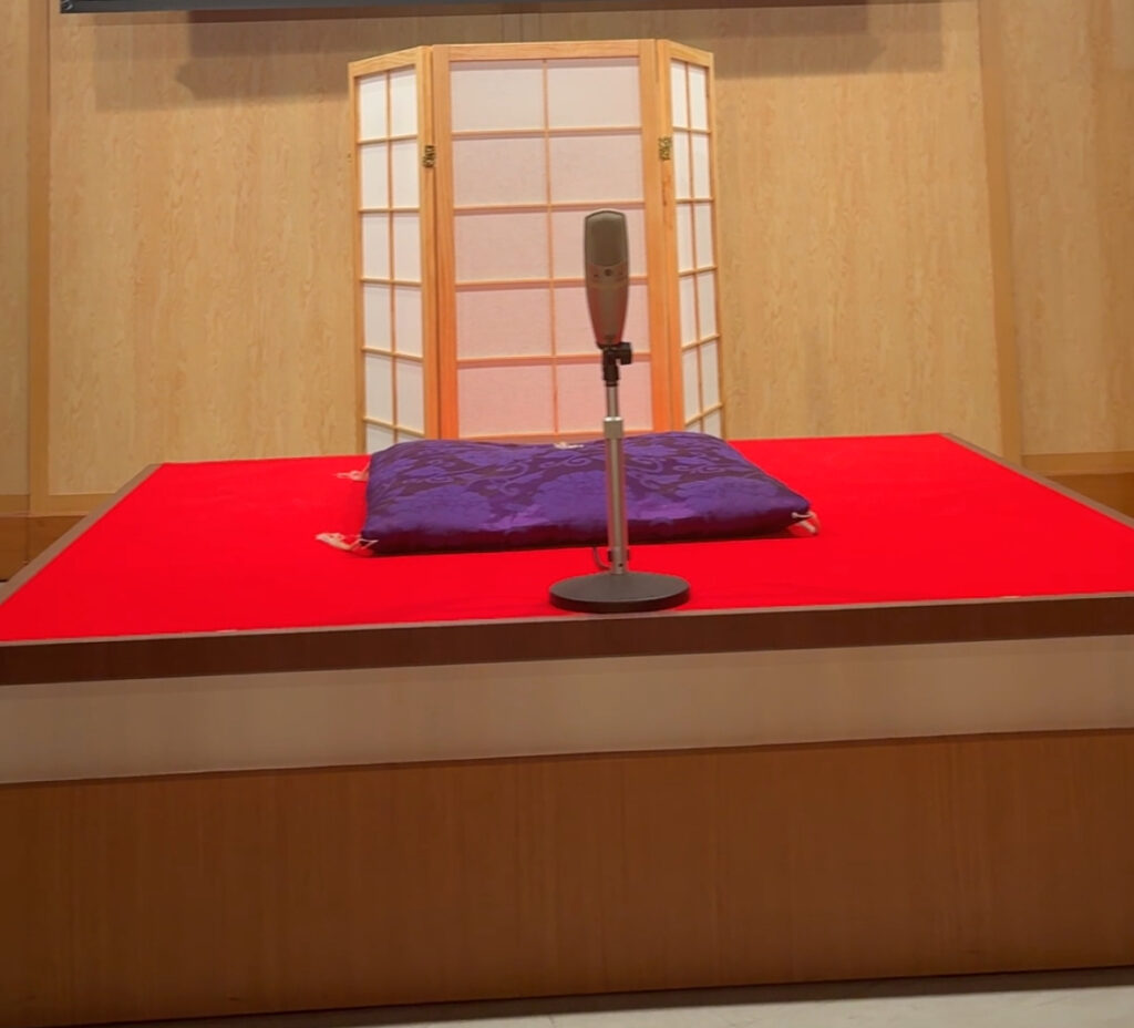 A cushion and microphone on a low stage with a folding screen backdrop, ready for the Rakugo performer.