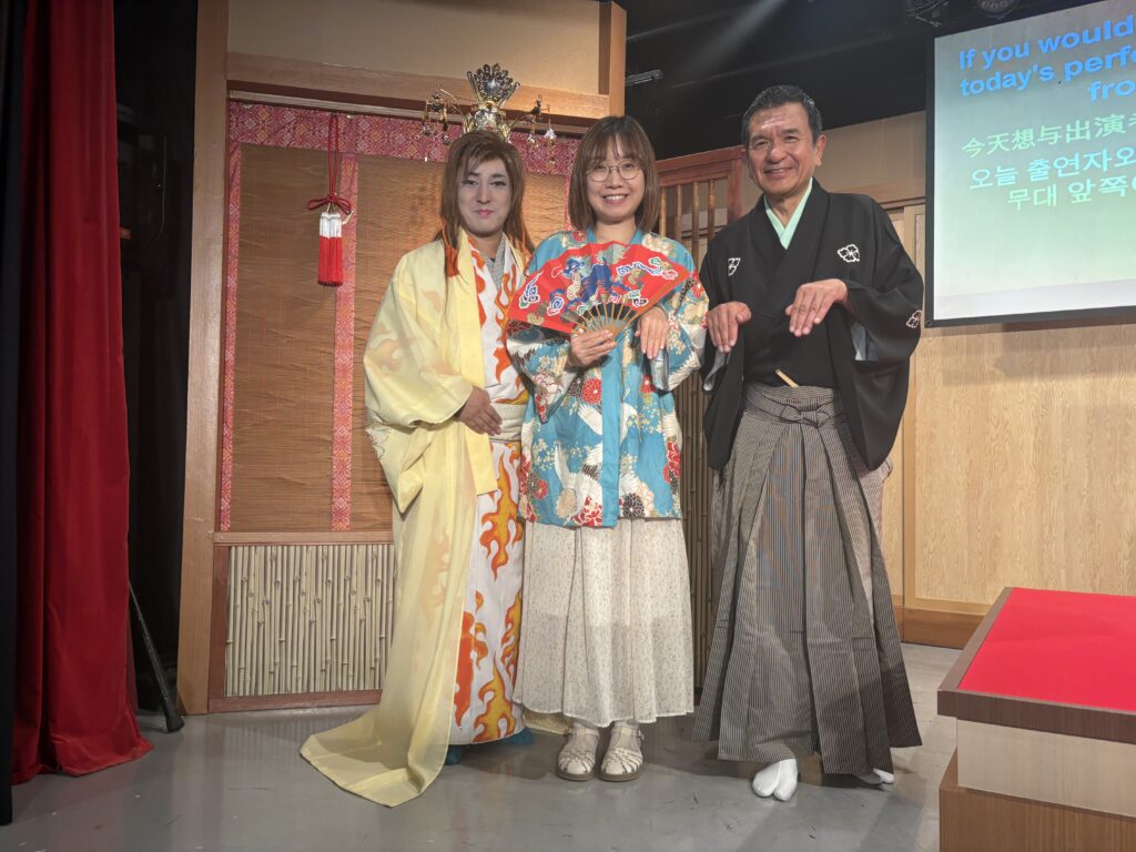 Audience member posing with two Rakugo performers in traditional costumes after the show.