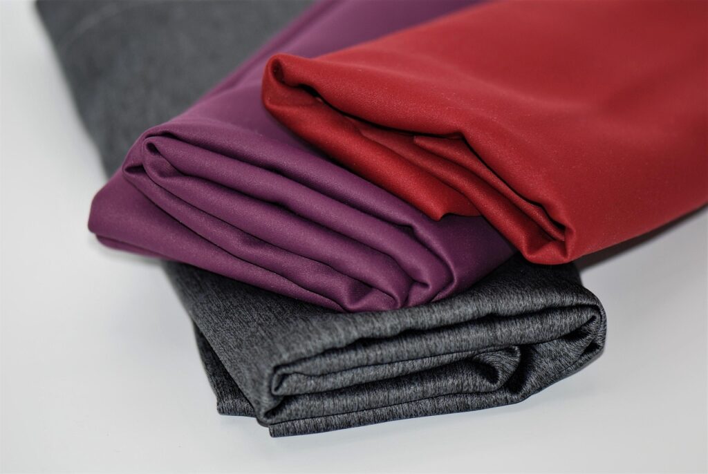 Neatly folded pieces of fabric in red, purple, and gray tones placed on a white surface.