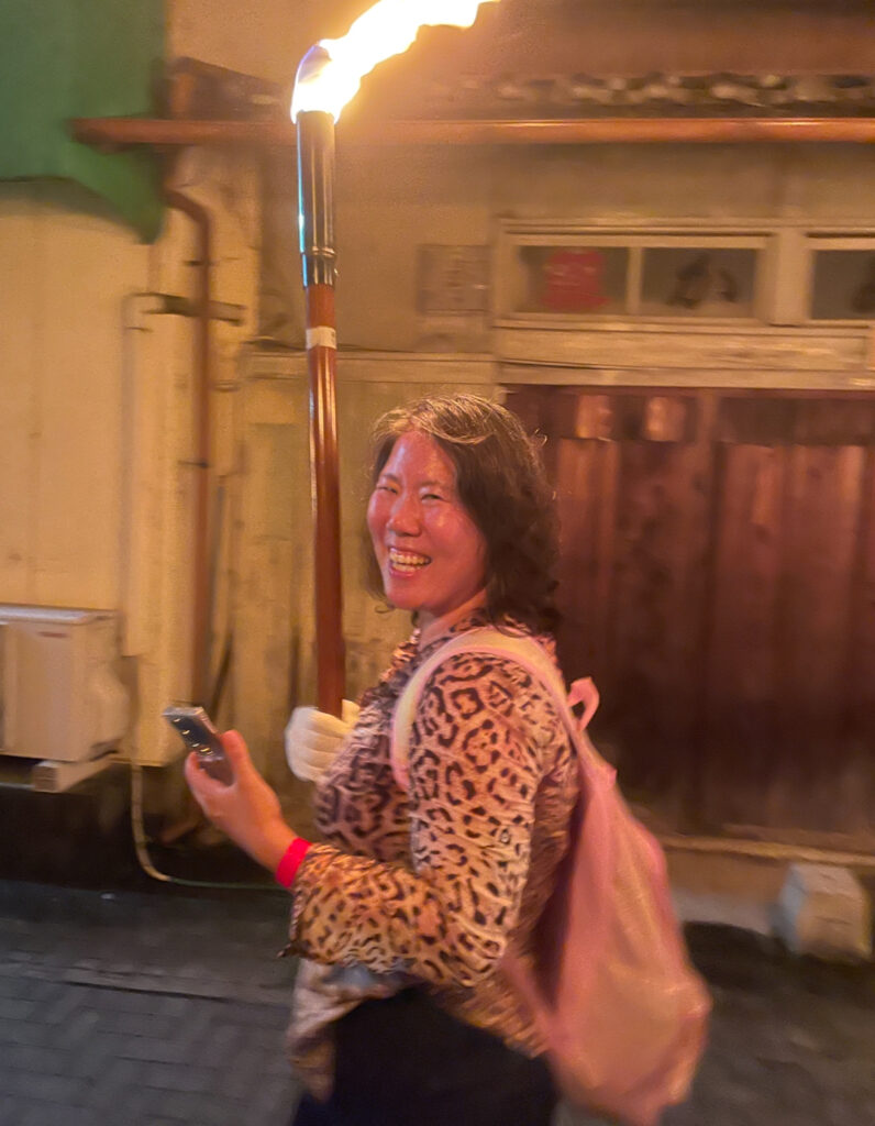 Woman smiling while carrying a fire torch during procession.