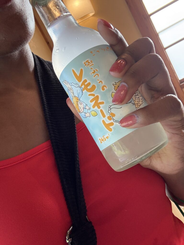 Close-up of a Ghibli-themed lemon soda bottle held by a visitor in a red top