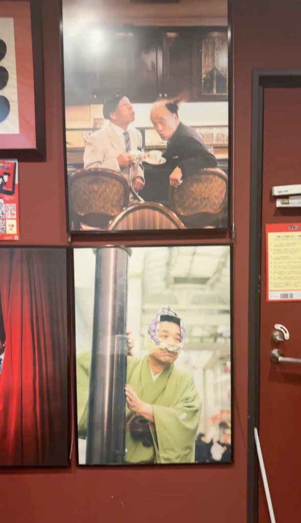 Framed pictures of Rakugo performers displayed on a red wall, showing humorous expressions and traditional costumes.