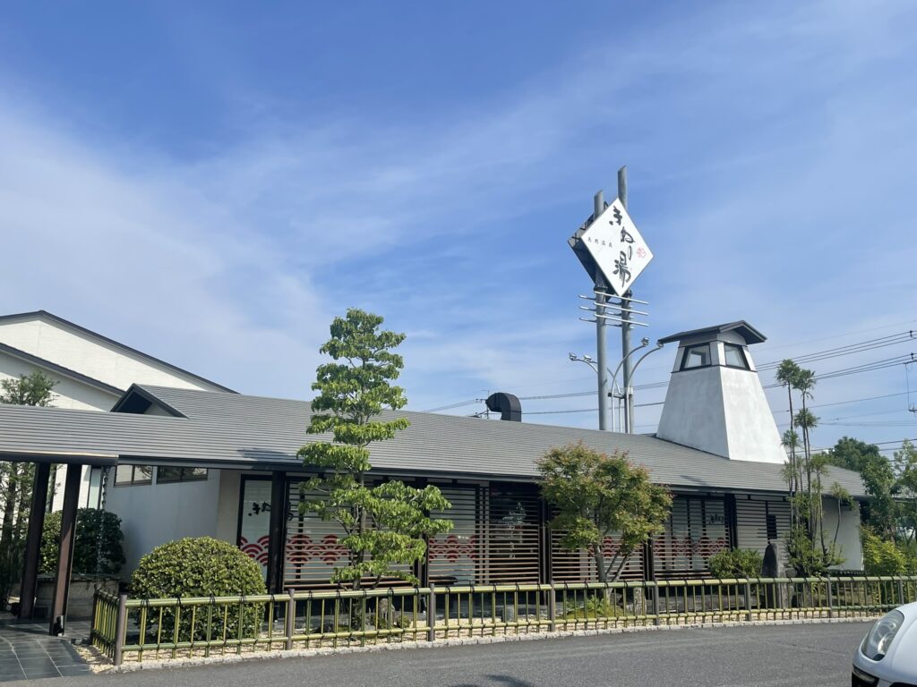 Exterior view of Kinu no Yu Villa in Chiba, a traditional-style bathhouse with a tall white sign and clear blue sky.