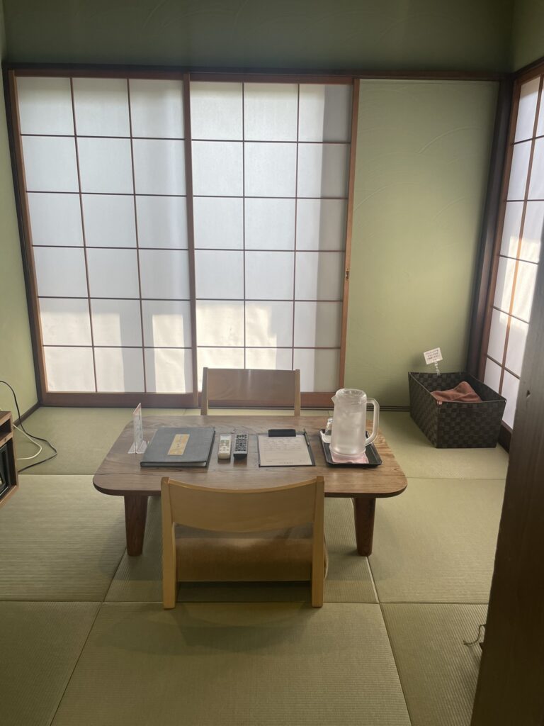 A tatami-style relaxation room at Kinu no Yu Villa, featuring low wooden chairs, a table with water pitcher, and sliding shoji doors.