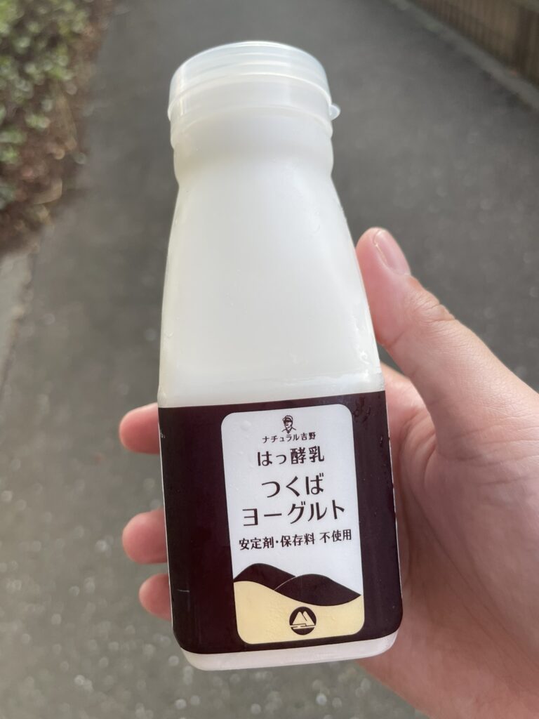 A hand holding a chilled bottle of Tsukuba yogurt drink, a popular refreshment after visiting an onsen in Japan.