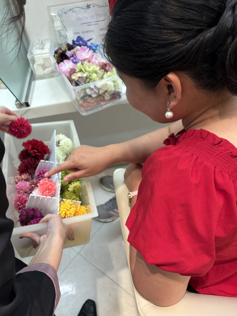 Woman pointing at a selection of artificial flowers while choosing hair accessories during her yukata preparation.