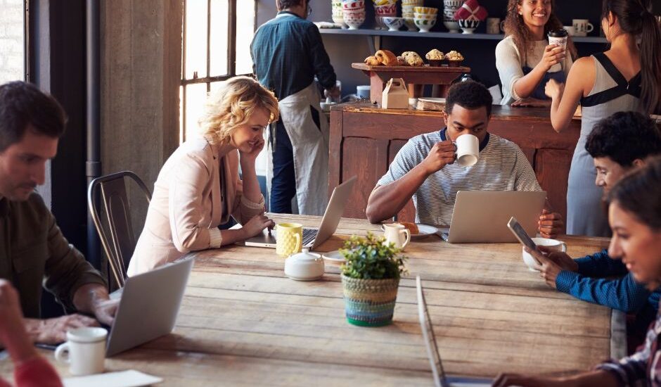 People working on laptops and drinking coffee inside a modern Tokyo café with communal tables.