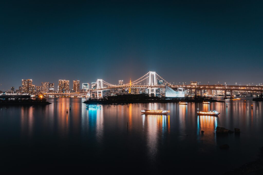 Illuminated cruise boats on Tokyo Bay at night with Rainbow Bridge and the Tokyo skyline glowing in the background.