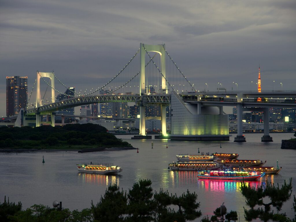 Traditional yakatabune pleasure boats lit with colorful lanterns cruising under Rainbow Bridge at dusk in Tokyo Bay.