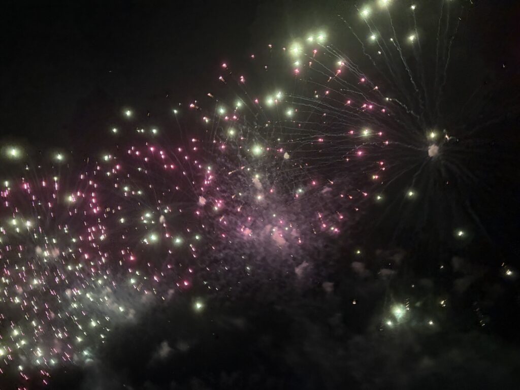 Vibrant pink and green fireworks bursting in the night sky over Tanabe.