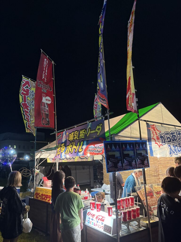 Festival food stalls selling colorful drinks and snacks at night.