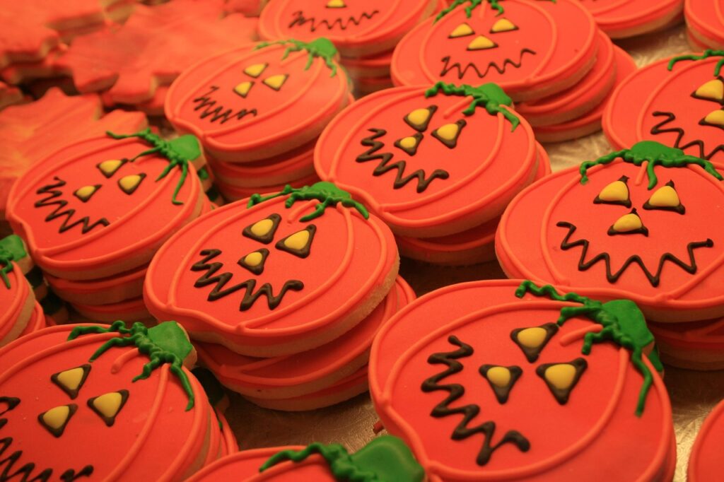 Rows of Halloween pumpkin cookies with orange icing, black faces, and green stems.